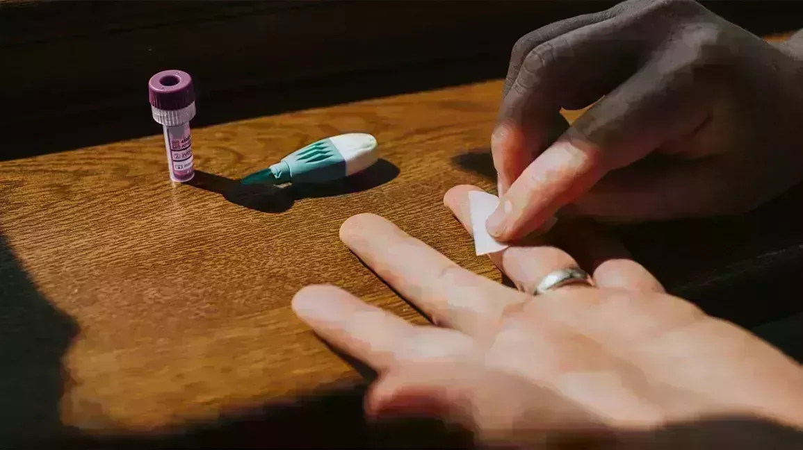 person wiping their left hand with an alcohol wipe, prepping to take an at-home hormone test kit. The vial and finger prick is to the left, above the left hand.