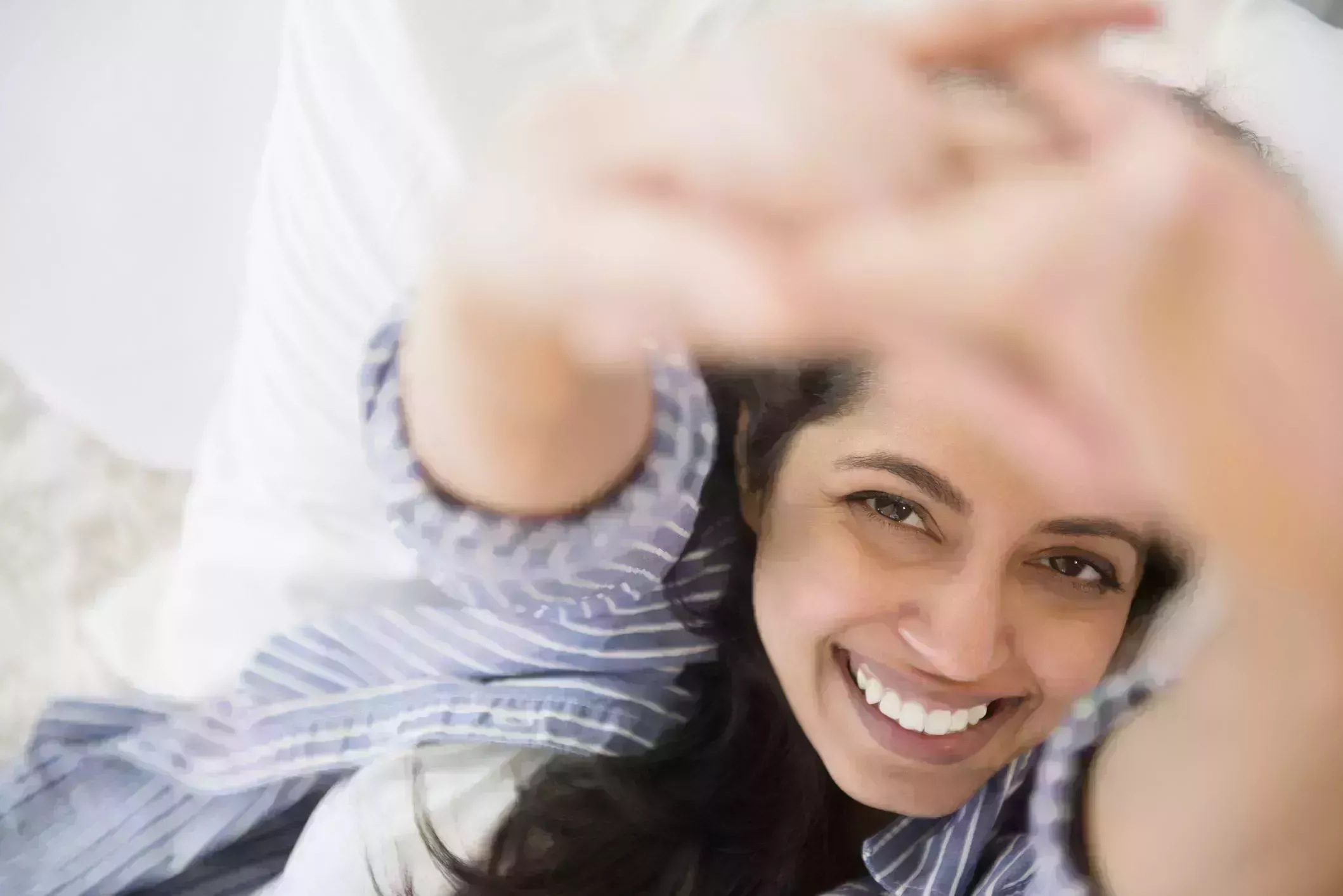 morning stretches – close up portrait of smiling asian woman laying in bed with fingers interlaced and arms stretched