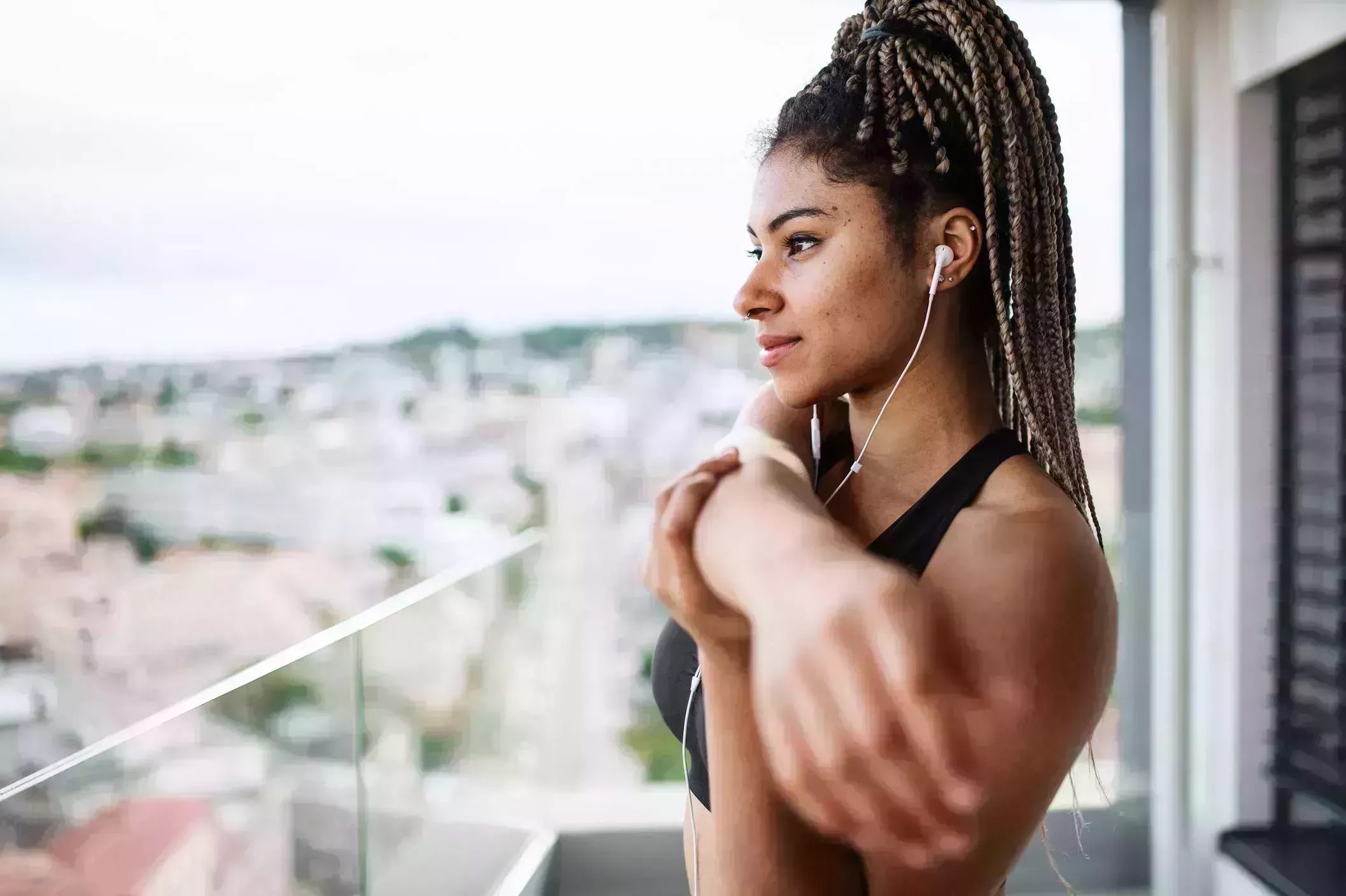 morning stretches – woman doing a cross body shoulder stretch on her balcony