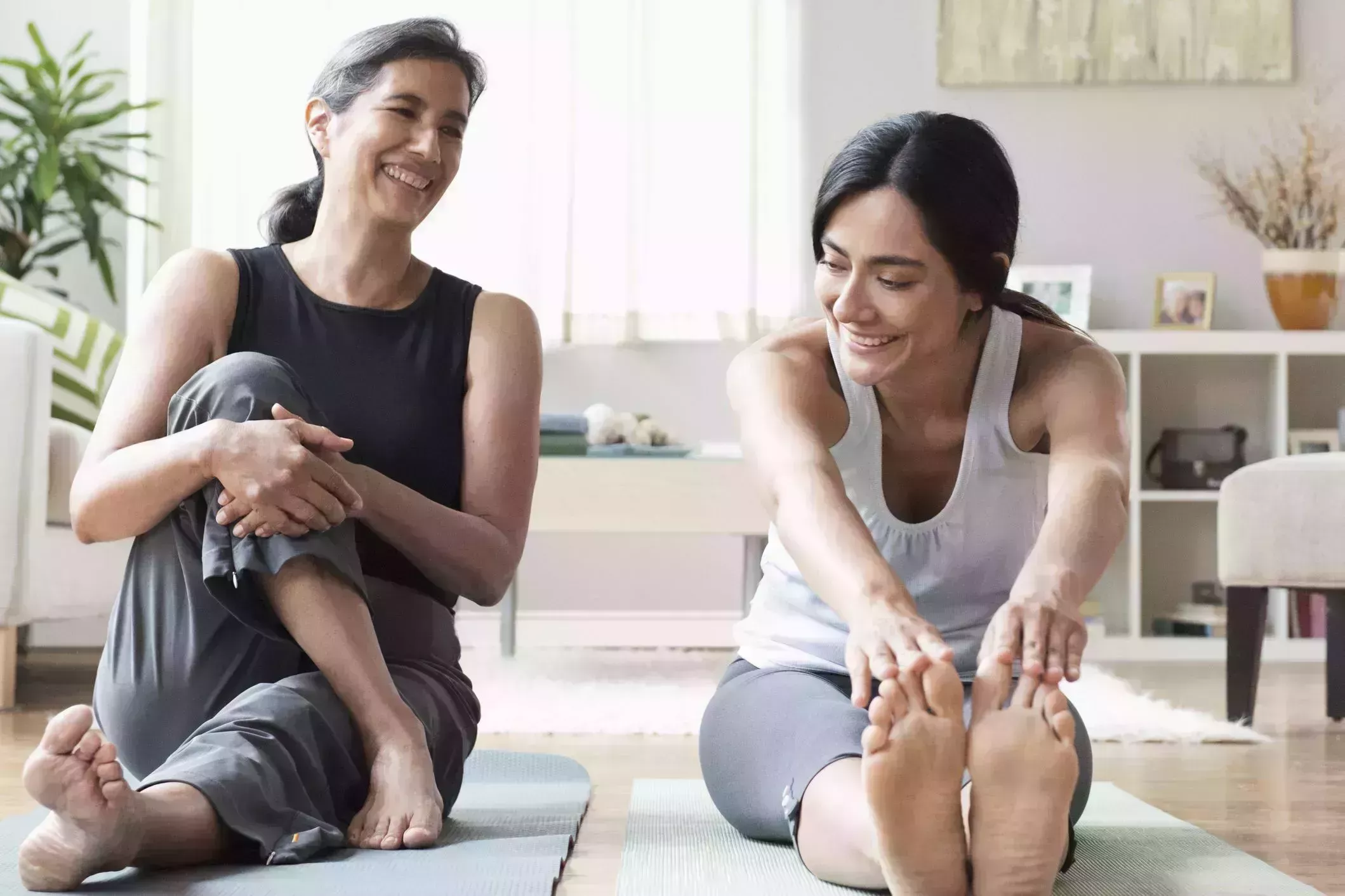 morning stretches – two women sitting on exercise mats with one doing a seated forward fold