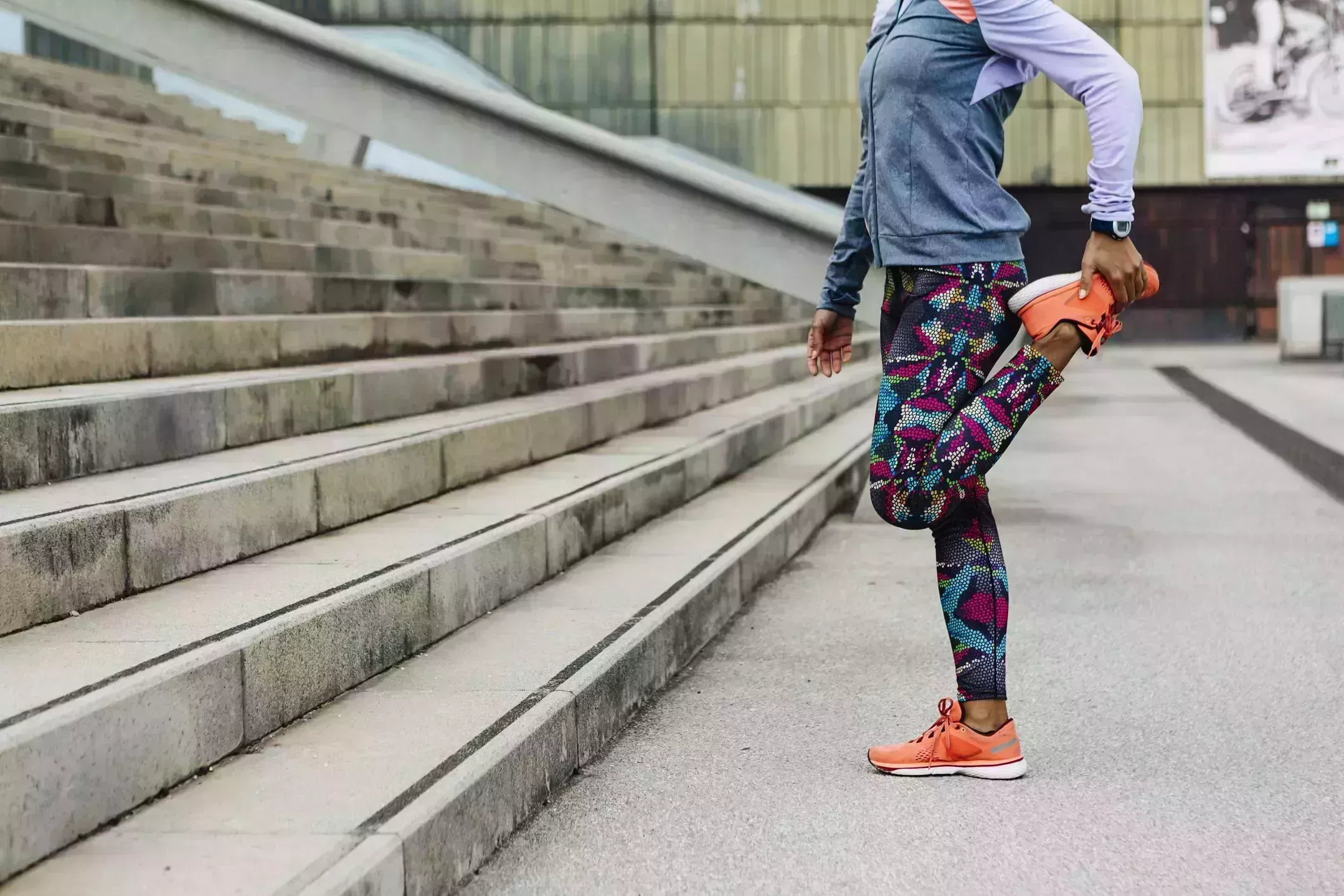 morning stretches – woman standing in front of outdoor stairs in workout clothes doing a quad stretch