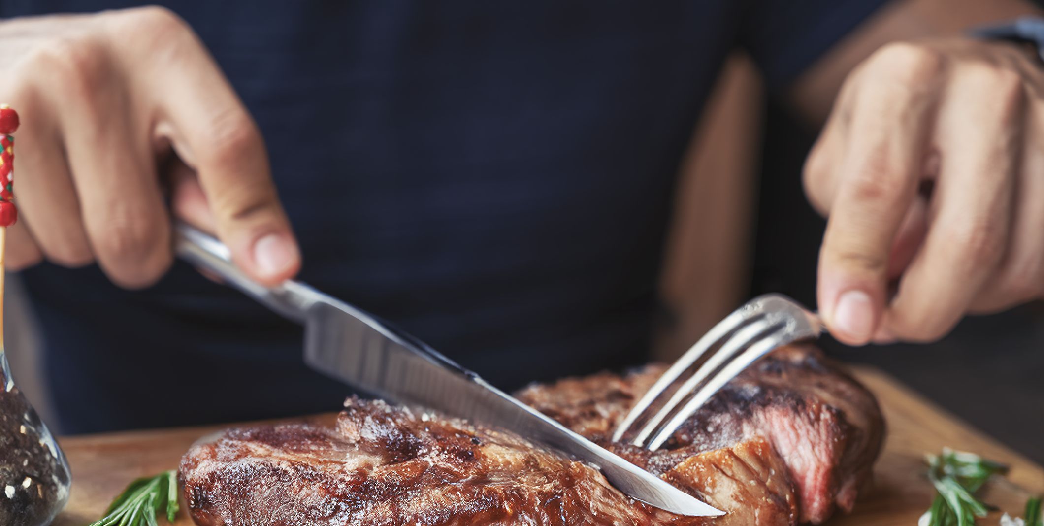 Men's hands holding knife and fork, cutting grilled steak